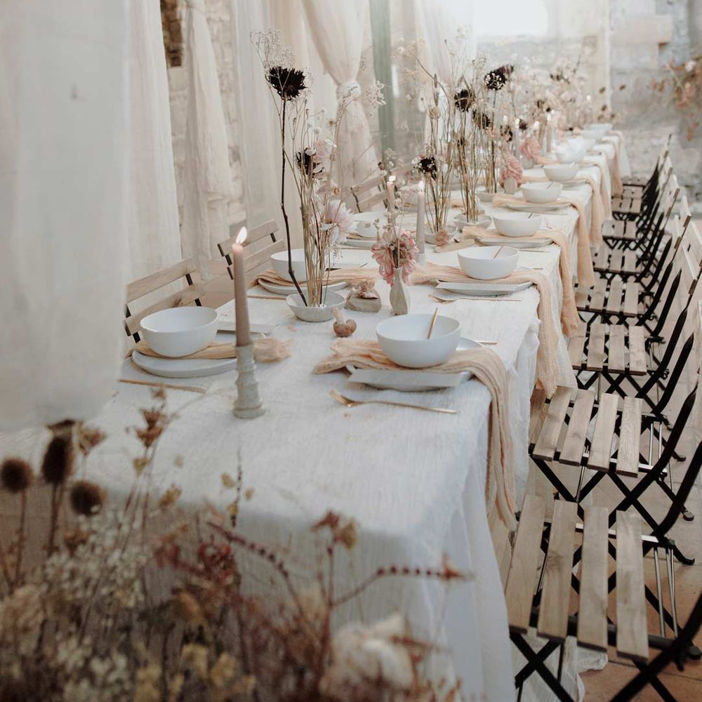 Neutral white minimal wedding tablescape with white table cloth, pink tulle napkins, black stems in vases and neutral tapered candles 