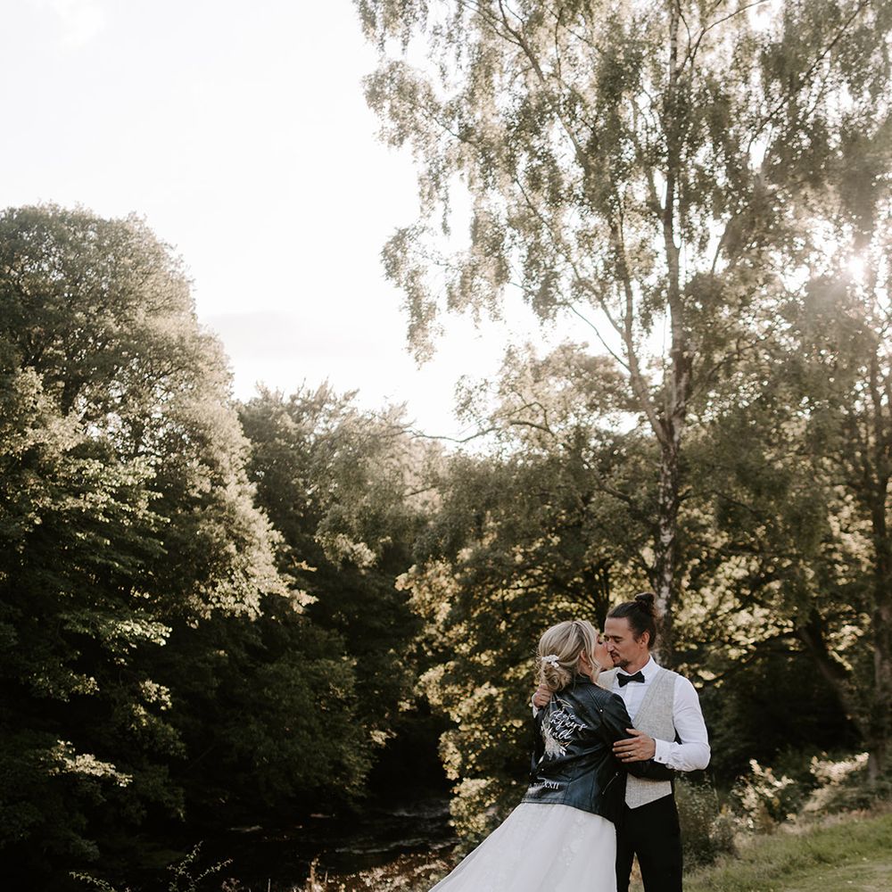 The bride in a long princess wedding dress from Eleganza Sposa with a personalised leather jacket cover up with the groom in light grey suit 