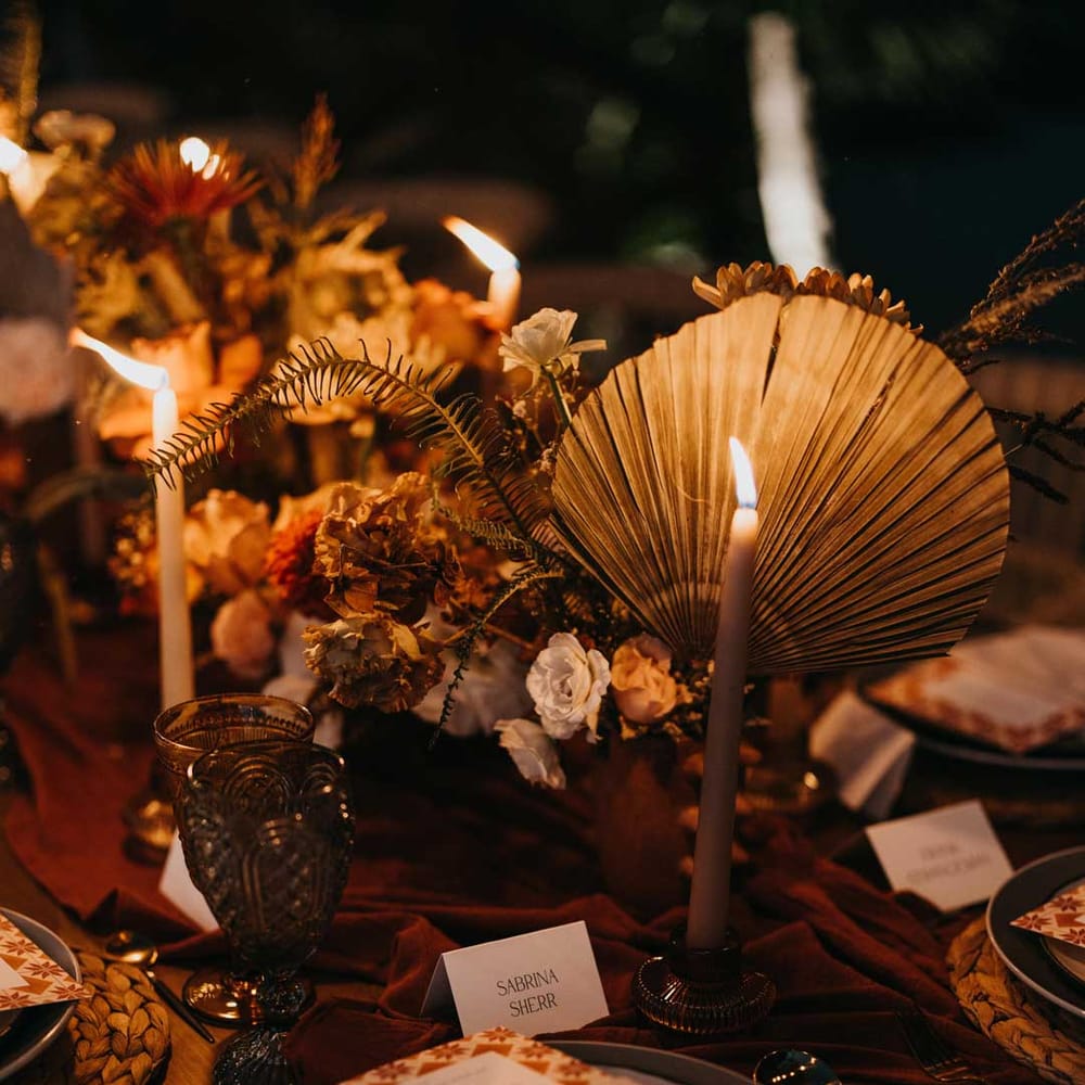 Rustic wedding tablescape with burnt orange dried roses, dried flower and foliage floral centrepieces, light orange tapered candles and burnt orange table runners