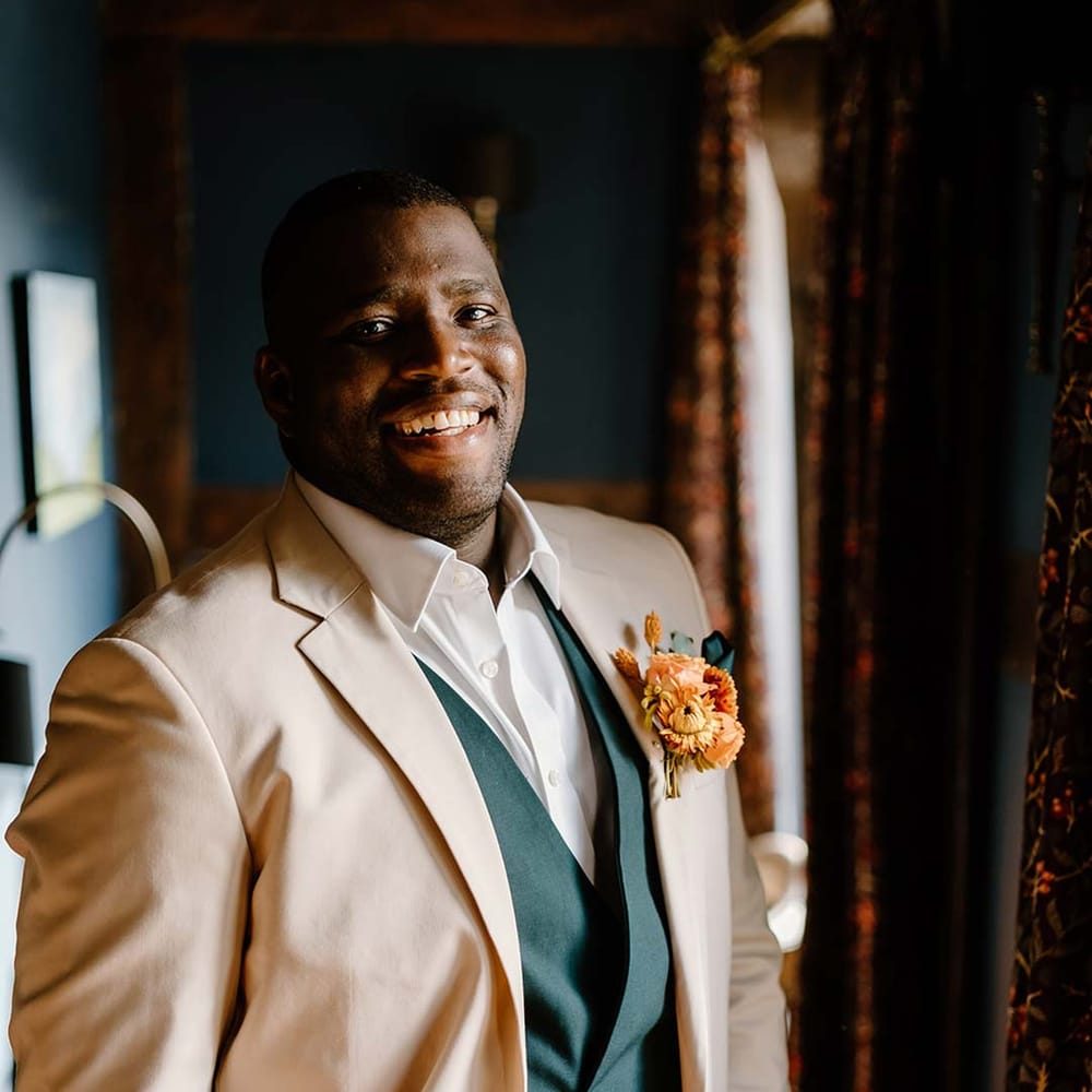Groom in cream grooms morning suit with forest green grooms waistcoat and trousers, forest green pocket square and orange boutonniere 