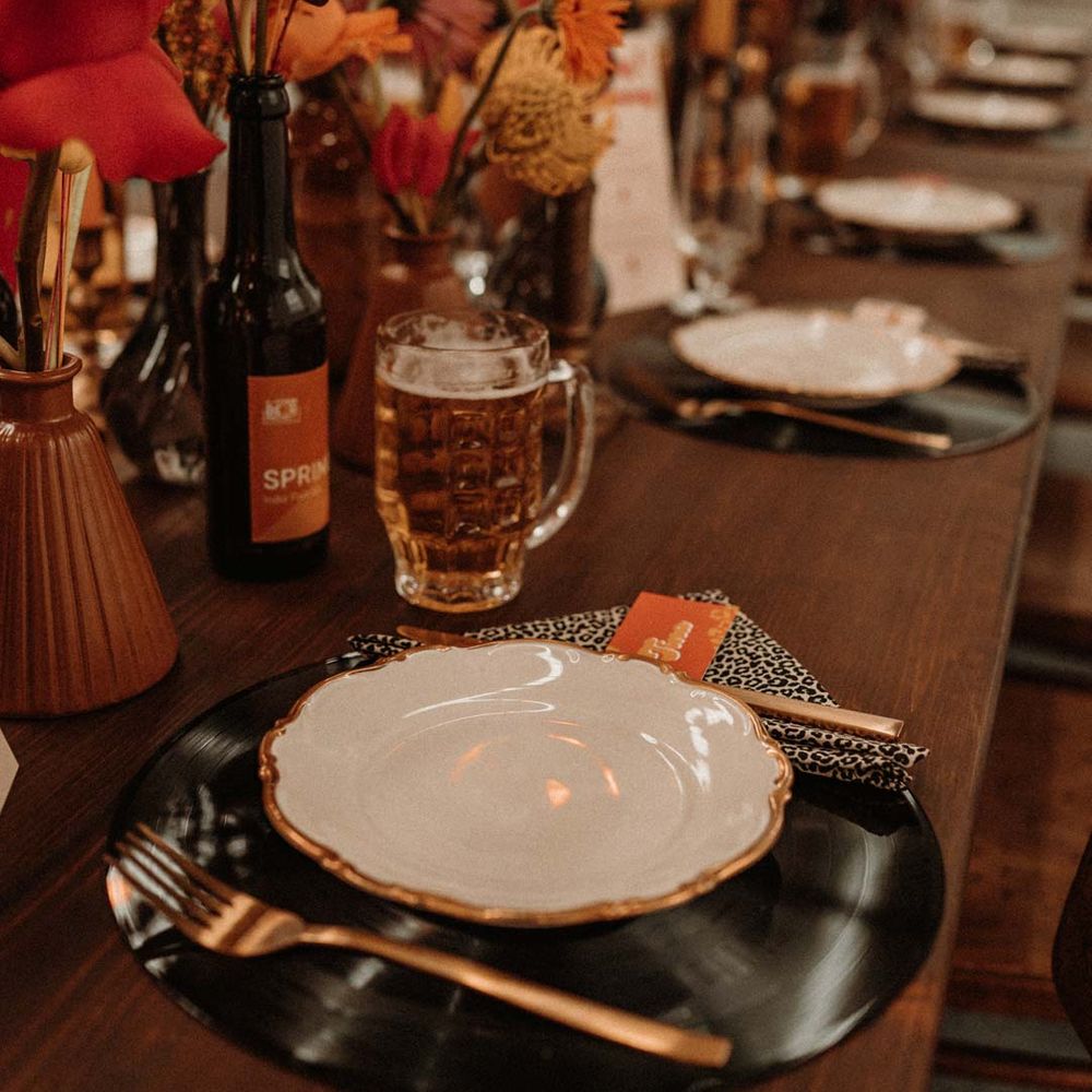 Rustic wedding tablescape with vinyl record place mats, gold rimmed plates, gold cutlery, colourful pink, red and orange floral centrepieces in bottles and tapered candles 