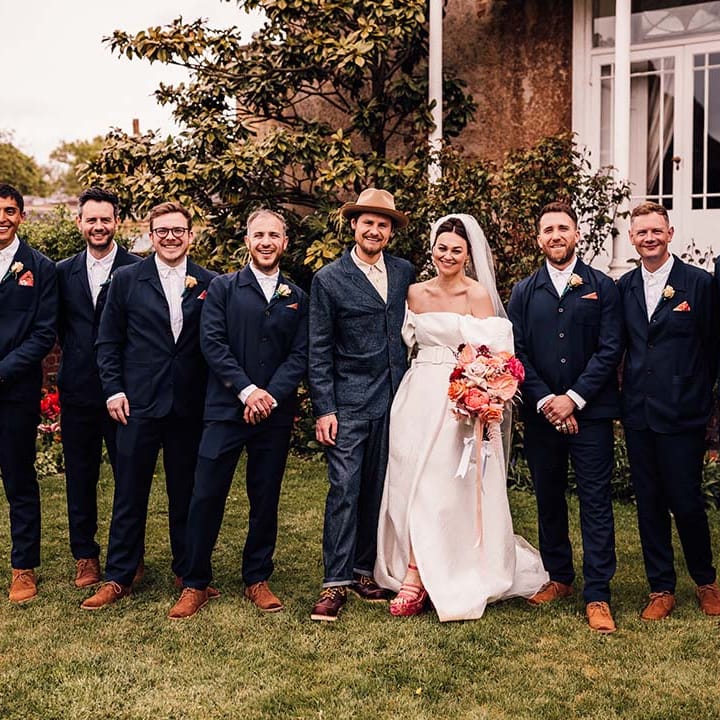 The groomsmen in navy suits posing with the bride and groom for large summer wedding 