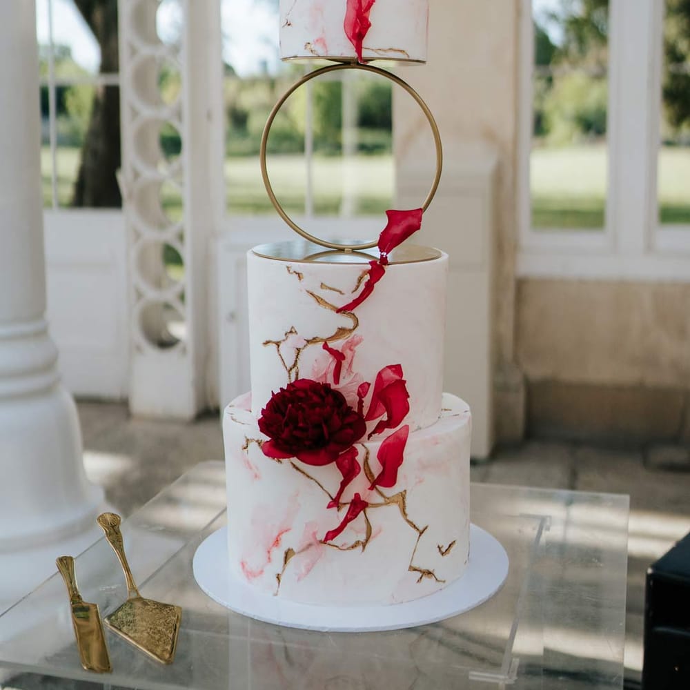 Artistic four tier wedding sculptural cake with hoop tier, gold icing, red icing and red rose decorations at Syon Park