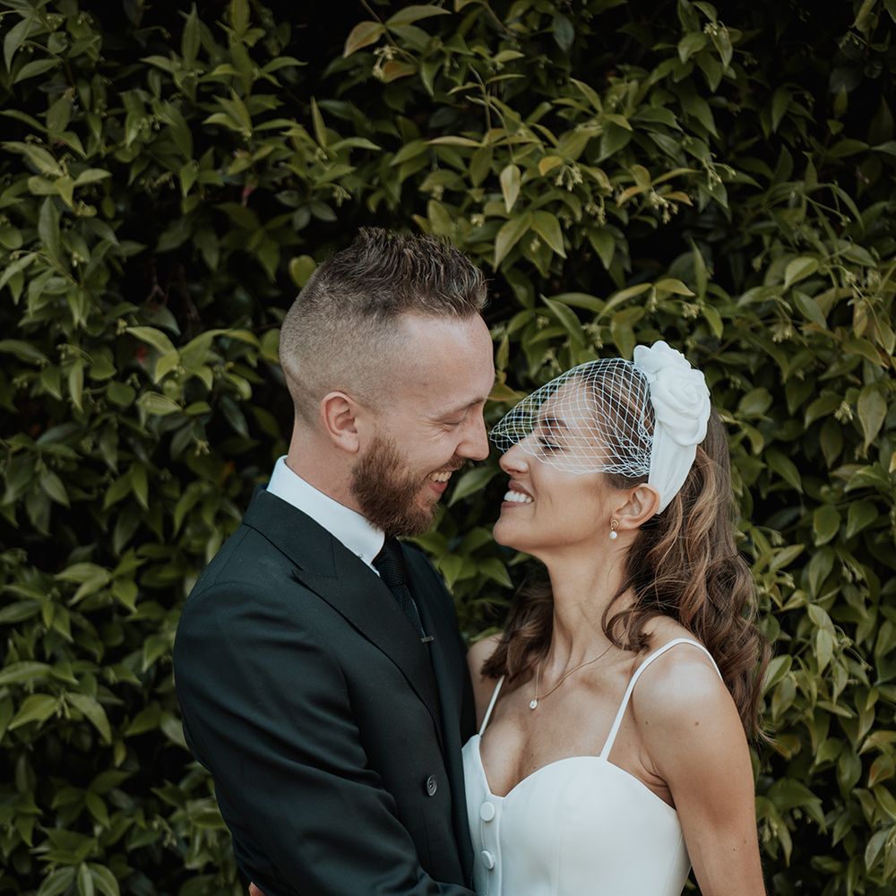 Groom in a black suit embracing his bride in a bridal top and skirt with birdcage veil at their stylish city wedding 