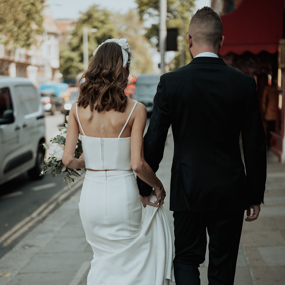groom in a black suit holding the skirt train for his bride in bridal separates at urban wedding 