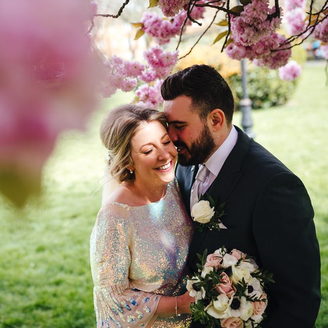 Bride & groom laugh together with blossom above their heads