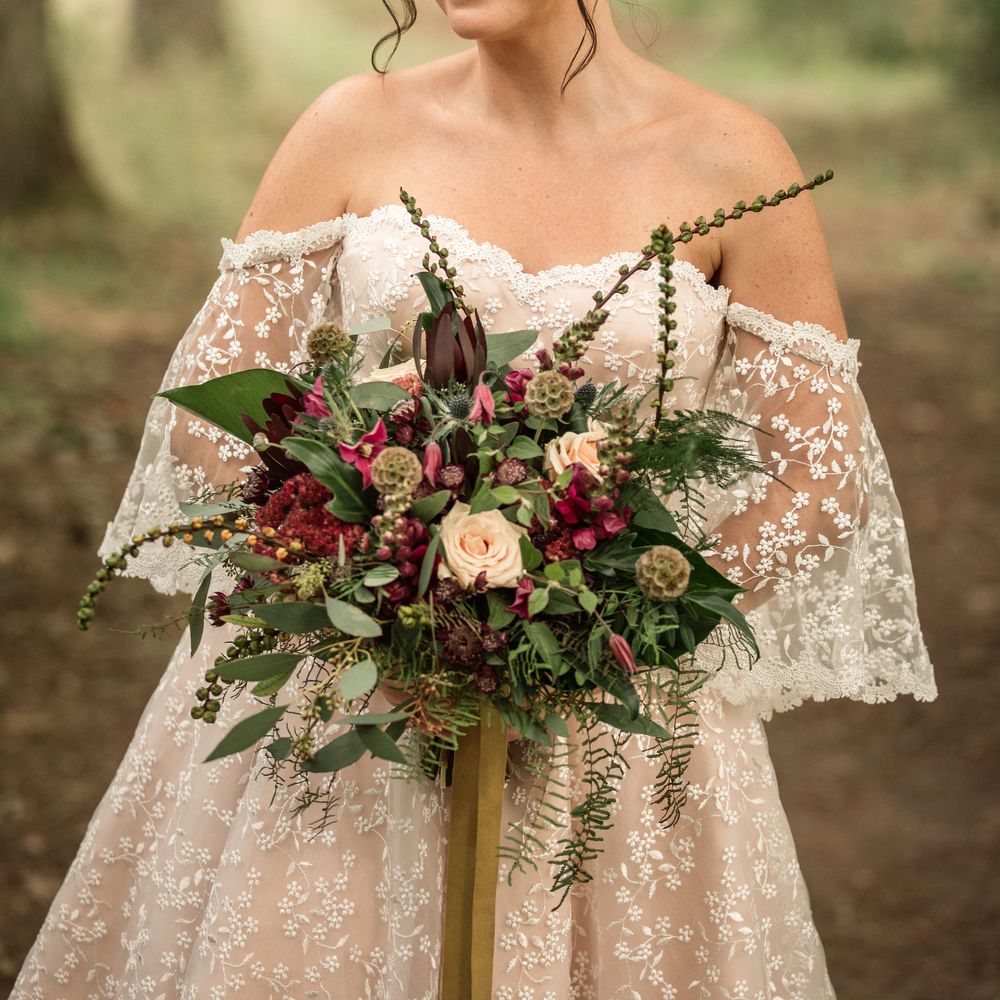 Bride stands wearing bridal gown and holds floral bouquet with pink blooms