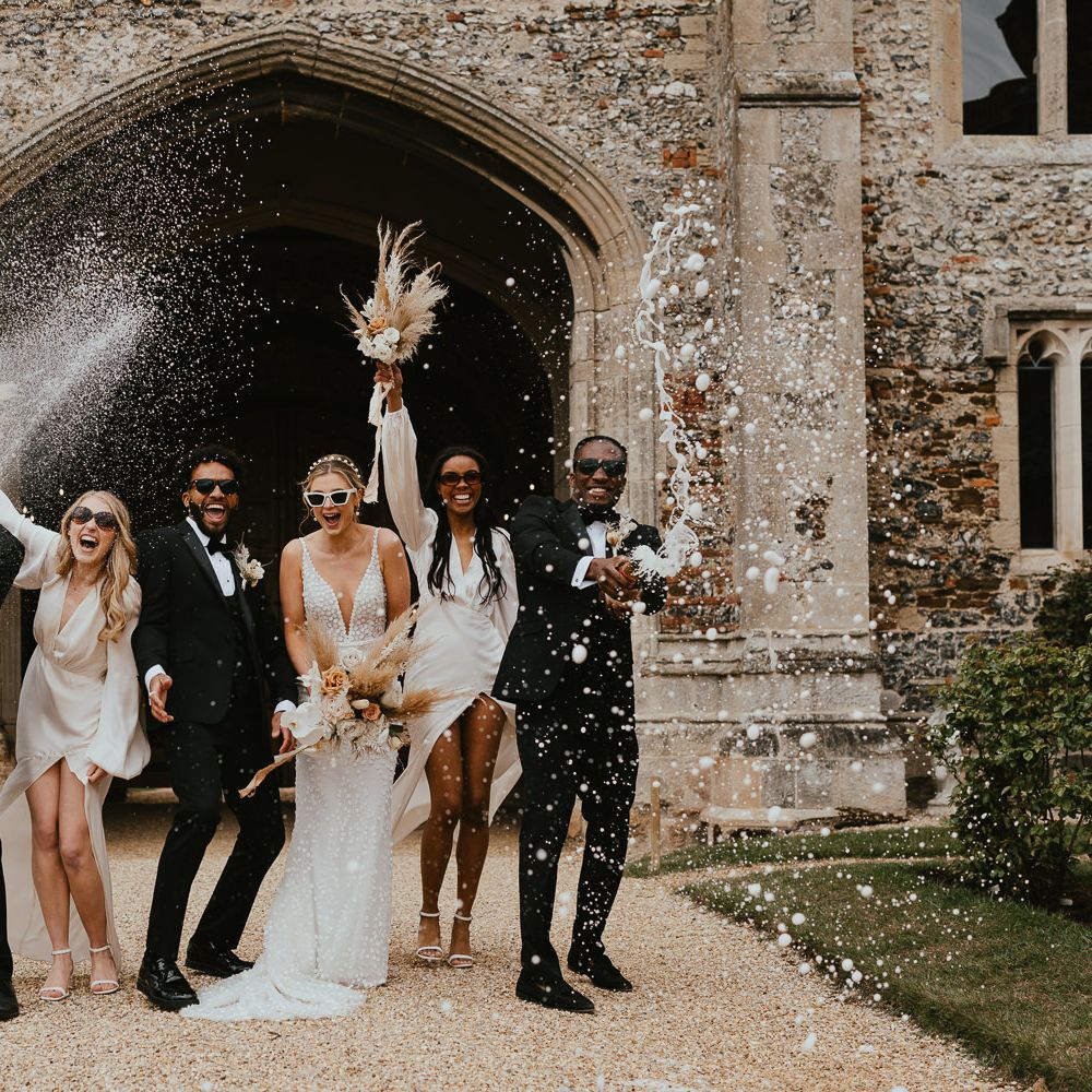 Fun wedding party portrait at modern luxury wedding with groomsmen popping and spraying champagne 