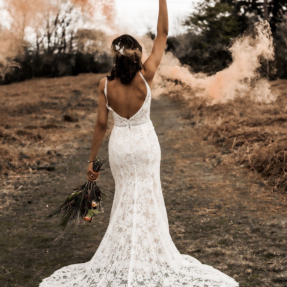 Bride in a fitted lace wedding dress with low back detail holding an orange smoke grenade 