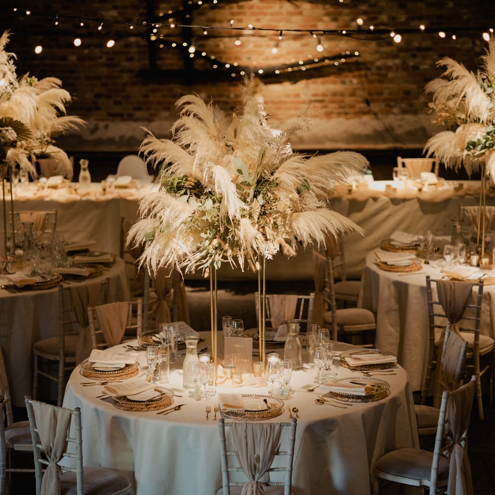 Round tables at Cooling Castle Barn wedding reception with tall pampas grass centrepiece decor 