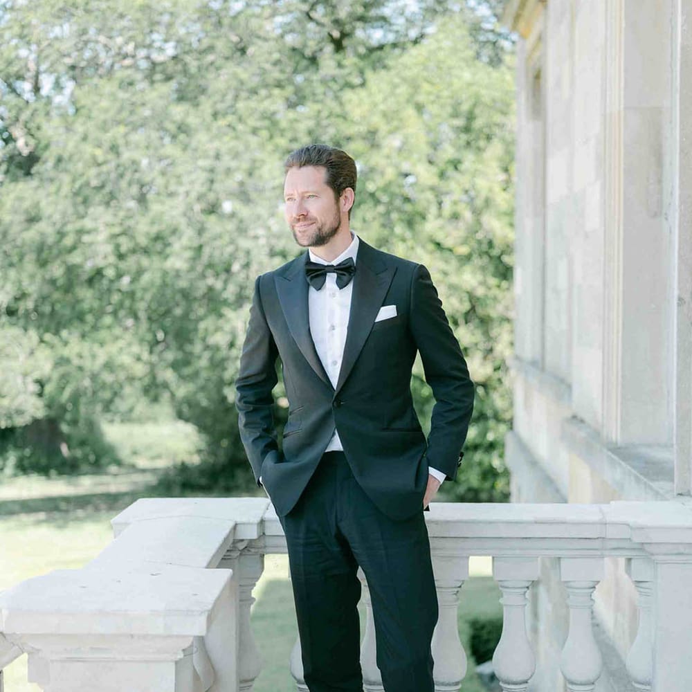 Groom in a black suit with bow tie standing on a balcony at Botley's Mansion in Surrey 