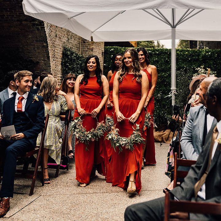 Bridal party in burnt orange bridesmaid dresses walking down the aisle holding foliage hoop bouquets at 100 Barrington wedding 