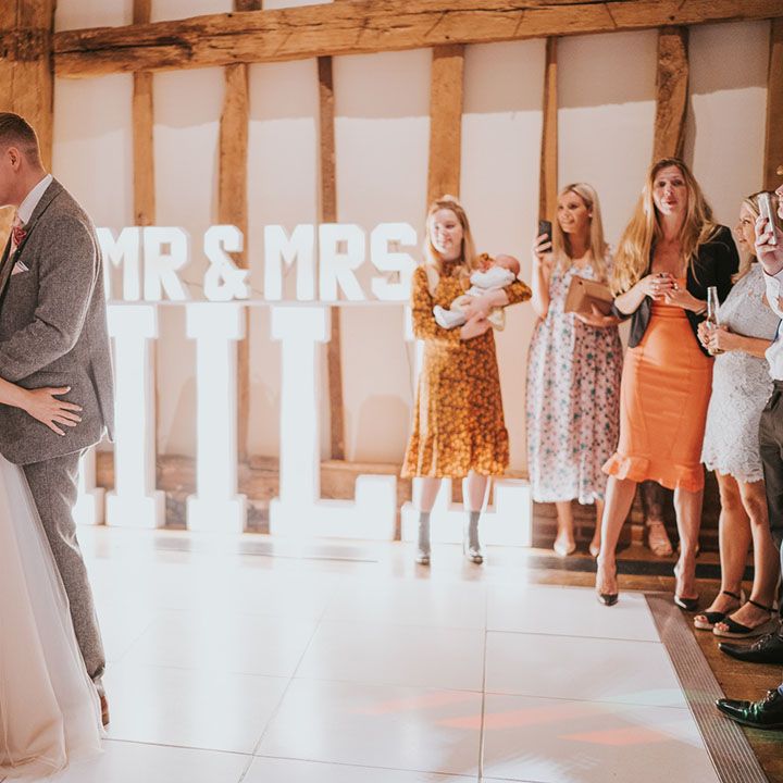 Bride and groom share their first dance on white dance floor in front of light up 'Mr & Mrs Hill' sign