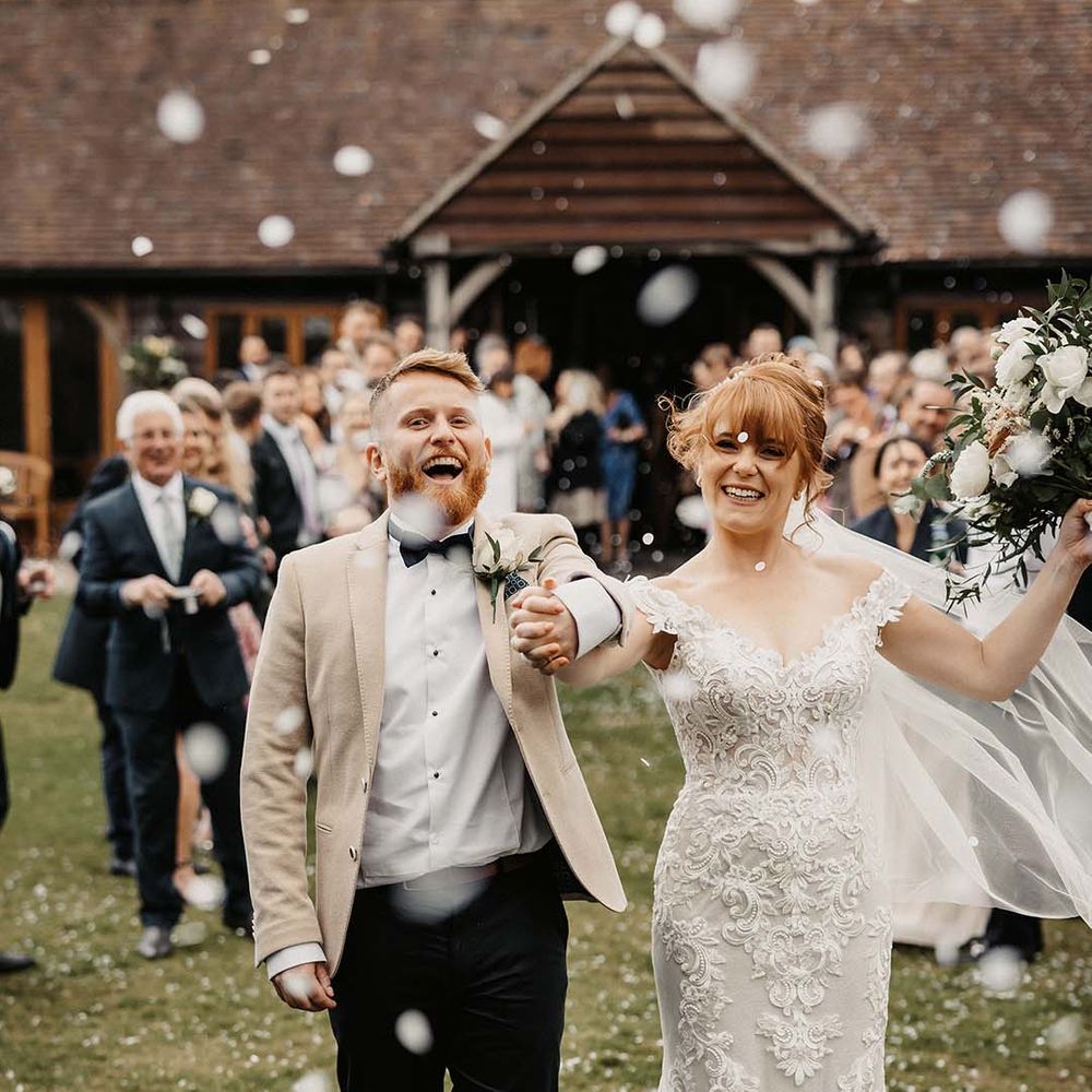 Bride and groom celebrate as they walk through confetti with white and orange wedding bouquet