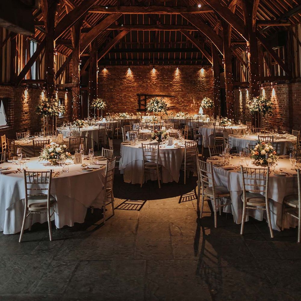 Wedding venue at Cooling Castle Barn with golden and white tables and white and orange flower decorations 