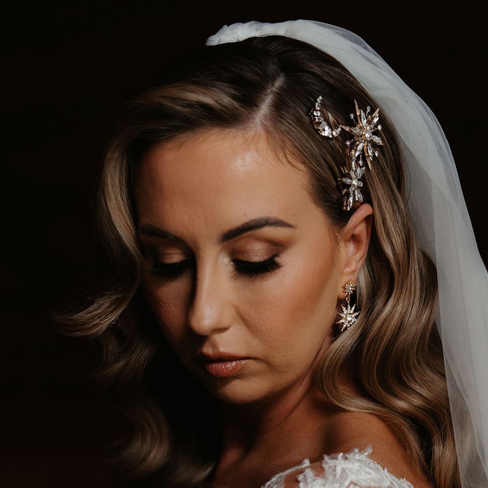 Bride with waved side swept hair has moon and stars gold and silver hair accessory with matching star earrings and veil