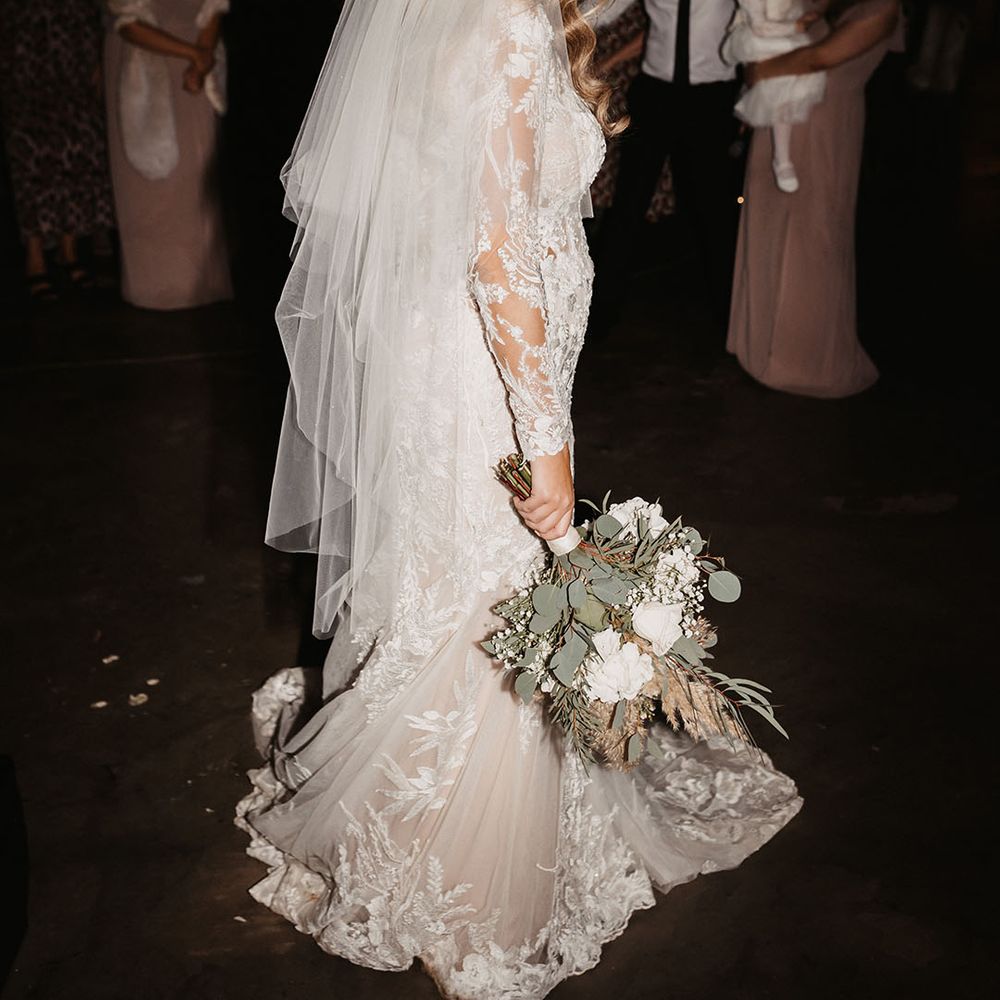 Bride in lace wedding dress and veil holds dried flower and white rose wedding bouquet 