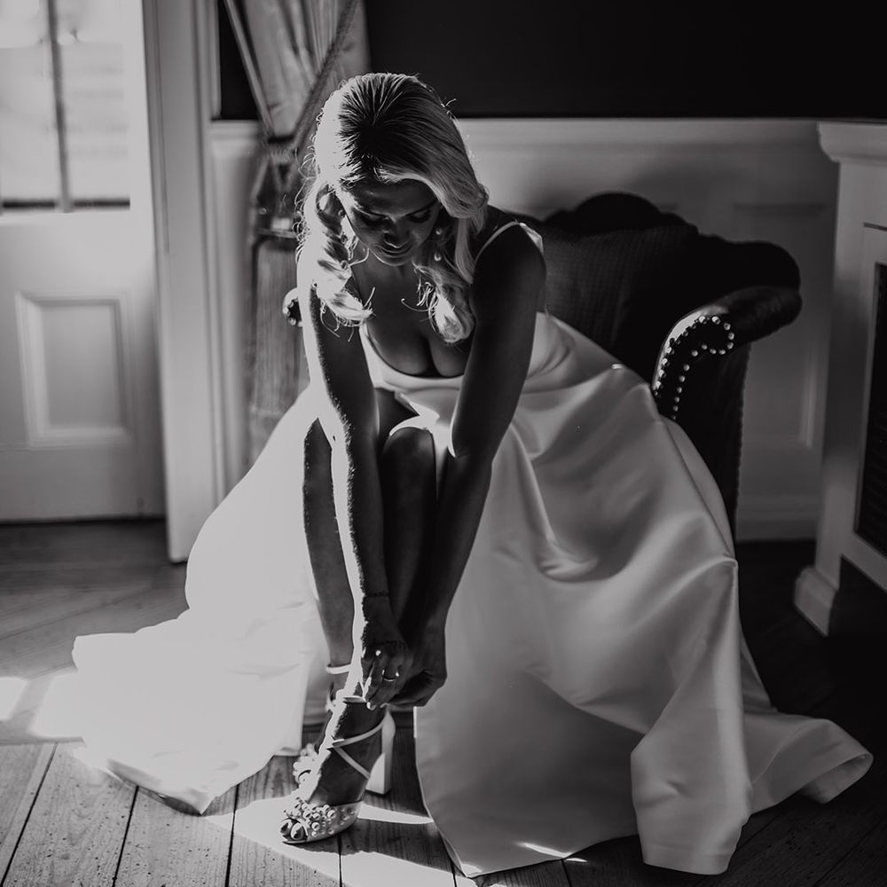 Bride in a princess wedding dress with side slit putting on her Charlotte Mills pear peep toe wedding shoes 