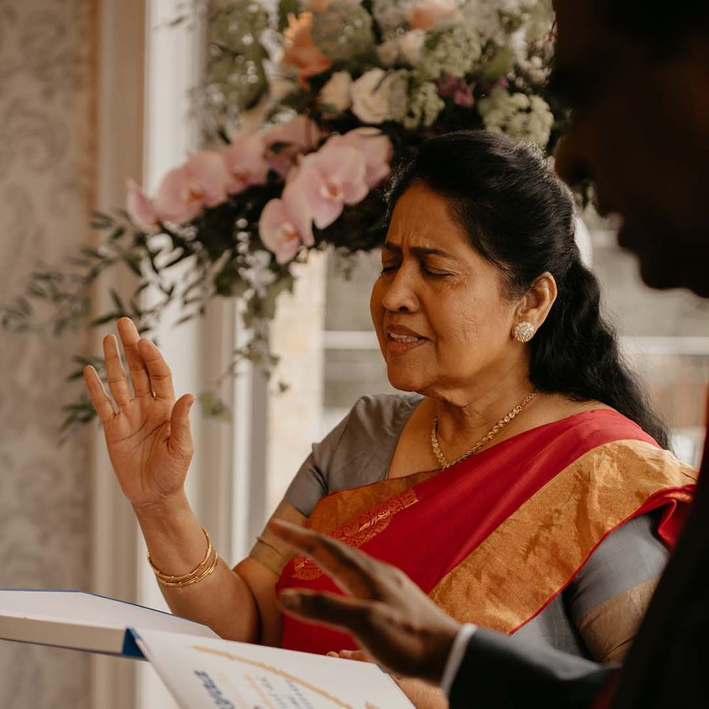 Guest in red and orange garment with golden jewellery, hand raised 