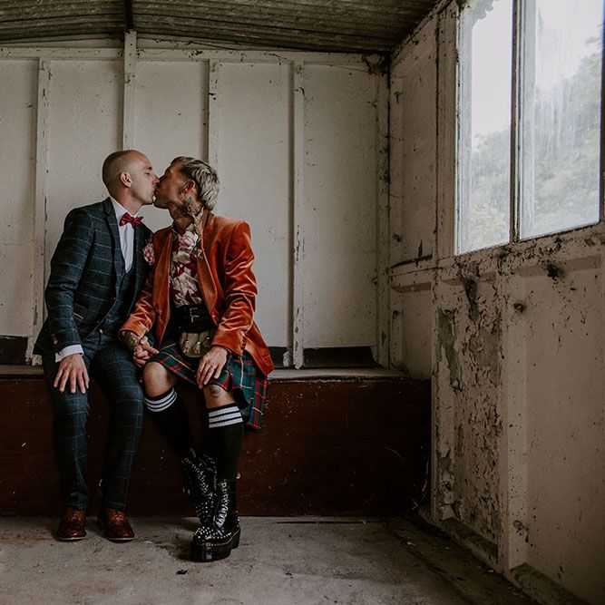 Groom wears orange velvet blazer and tartan kilt next to his groom who wears tartan suit complete with red bow tie 