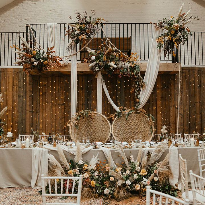 Autumnal orange and warm toned wedding flowers with pampas grass decorate the top table with peacock chairs 