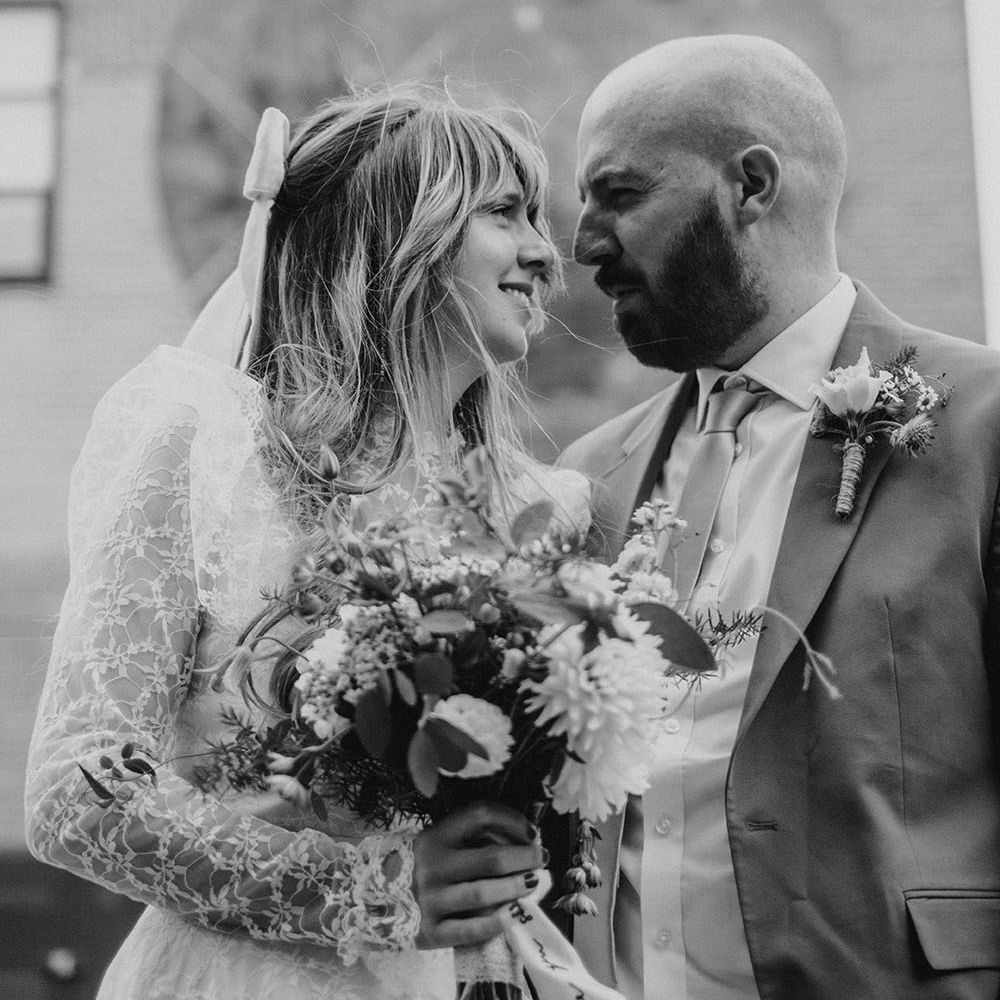 Bride with bow in her hair looks lovingly toward her groom after intimate civil ceremony in Liverpool 