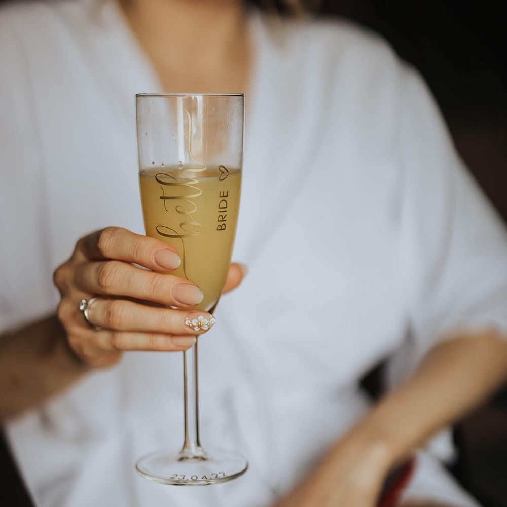 Bride holds a personalised champagne flute with simple wedding nails with a flower accent nail design 