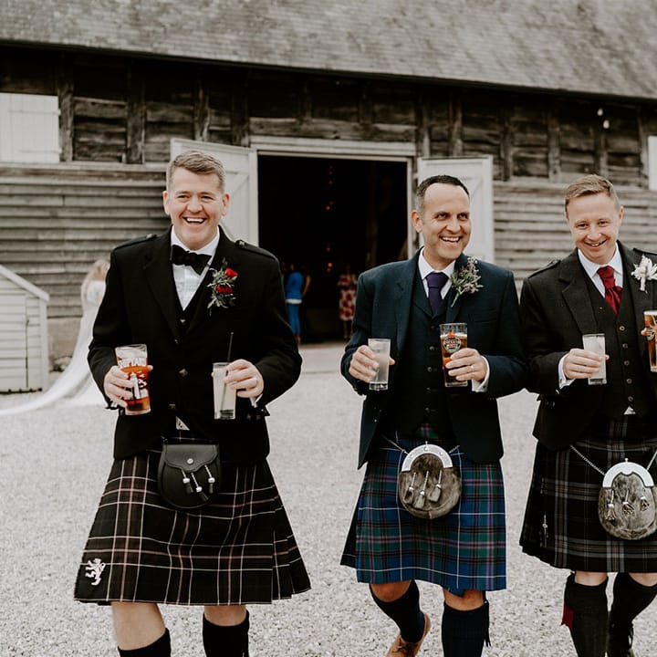 Groomsmen in traditional Scottish kilts walking with their pints at Pimhill Barn wedding reception 