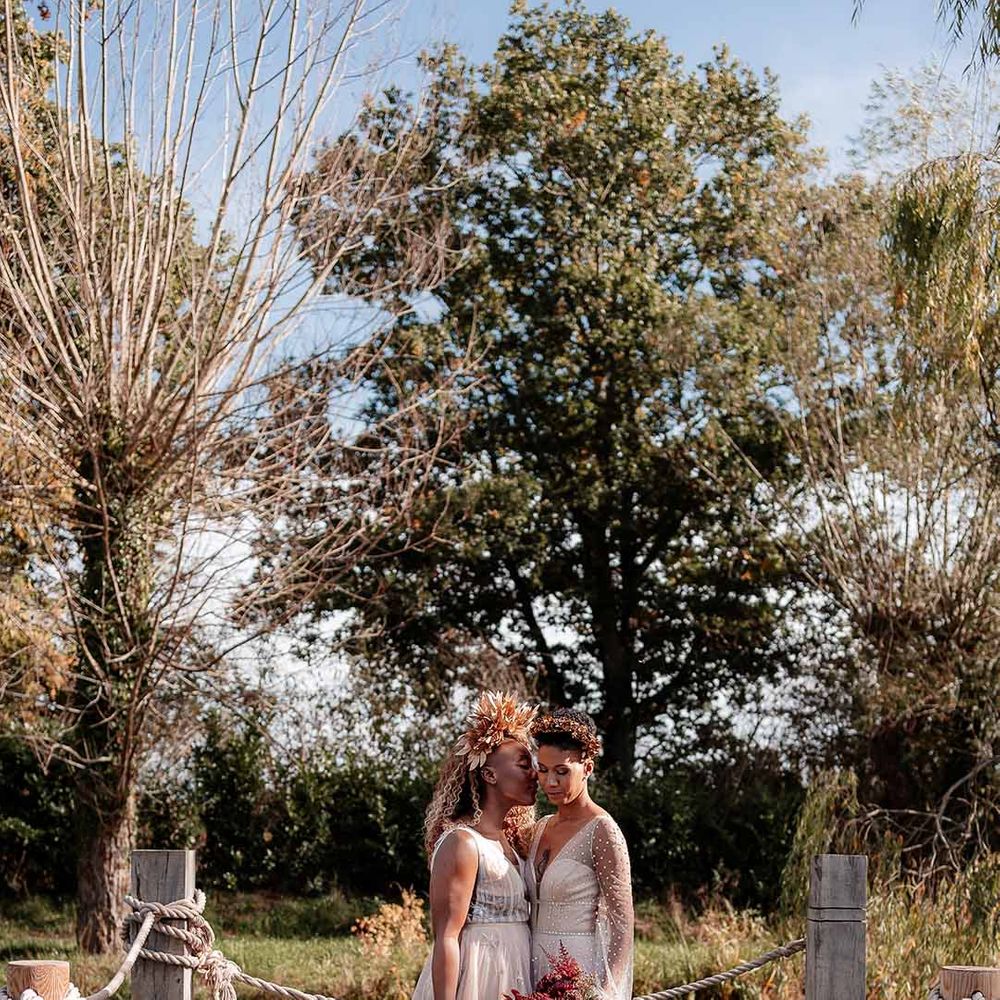 Brides in complimenting ethereal boho wedding gowns and large autumnal dried flower bouquets embracing at Silchester Farm