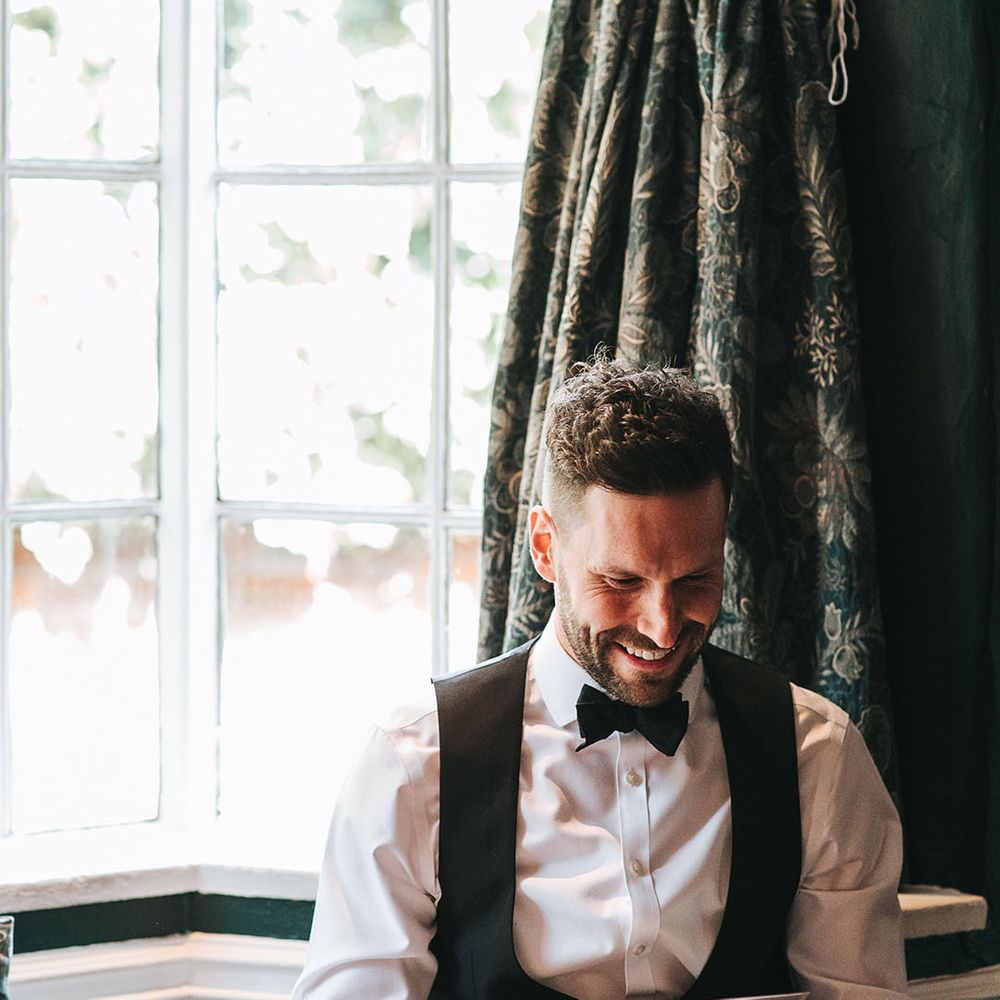 Groom smiles as he opens up a personal letter in black tie on the morning of the wedding 
