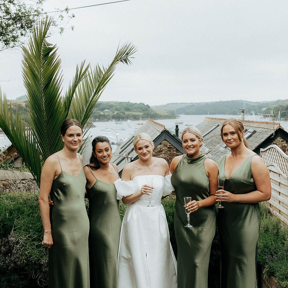 Bride stands with her bridesmaids in different styled satin green bridesmaid dresses 