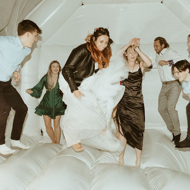Bride in personalised leather jacket jumping on the bouncy castle with some wedding guests during the wedding reception 