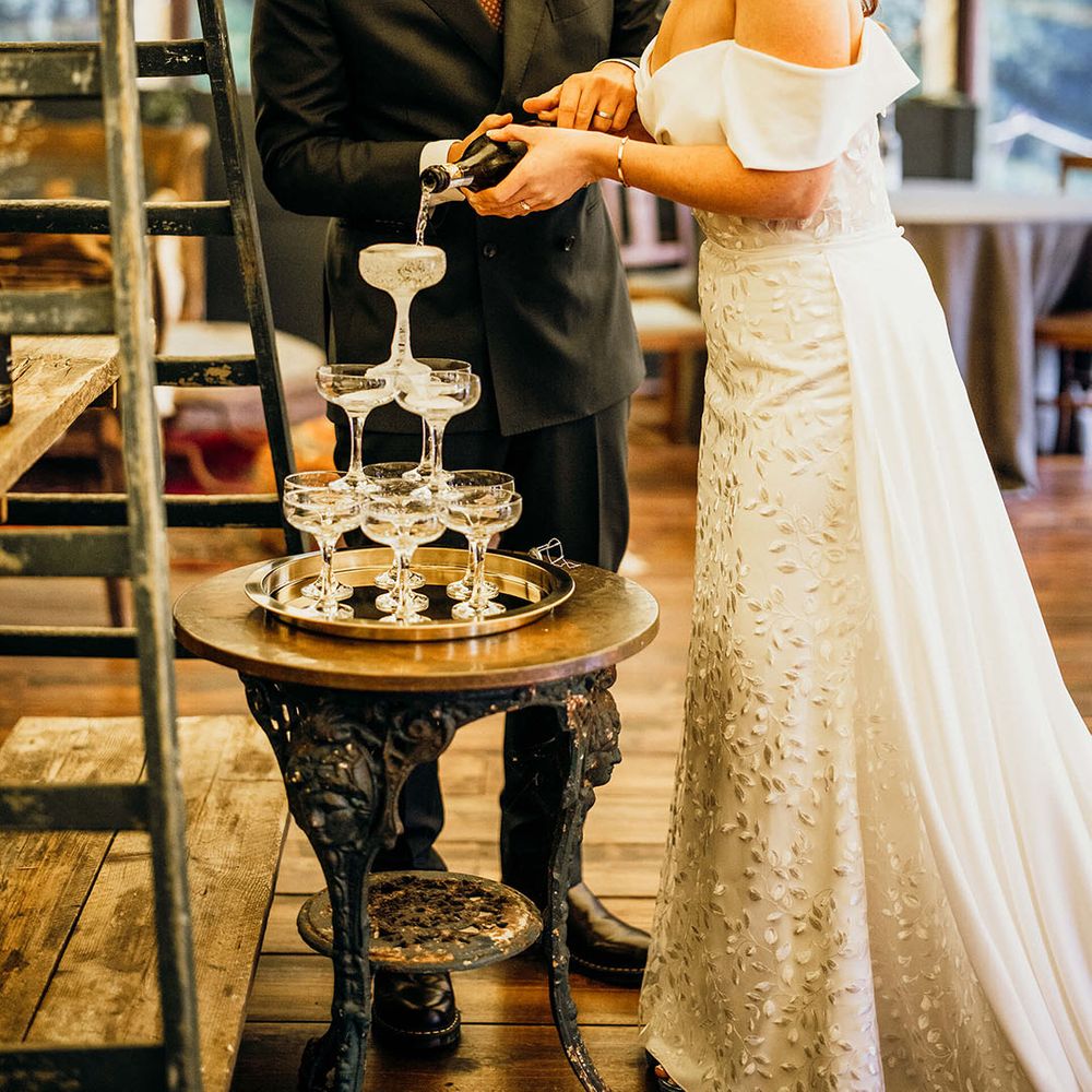 Bride & groom pour champagne into champagne tower