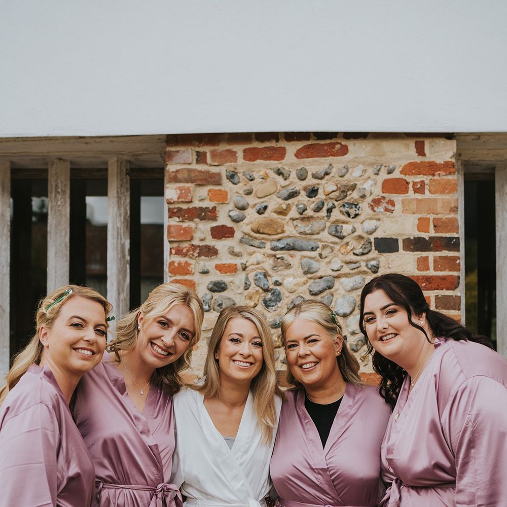 Bridal party with the bridesmaids in pink satin robes and bridesmaids in white satin robe as they all get ready for the wedding day 