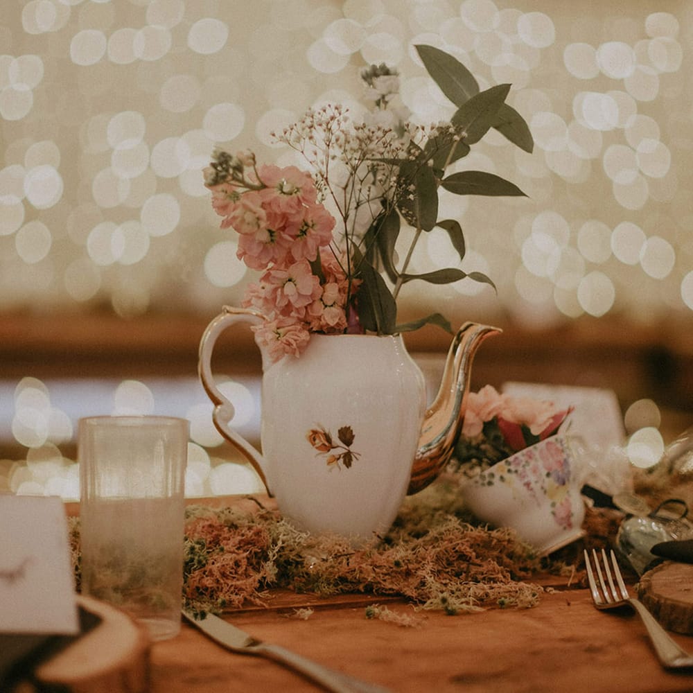 Antique teapots and teacups filled with pink flowers with moss acting as the table runner for outdoor boho wedding 