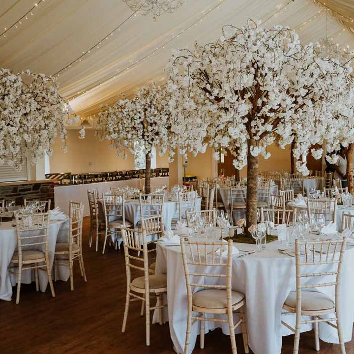 Simple classic white and grey wedding tablescape in wedding marquee with fairylights and faux decorative trees at Tredudwell Manor