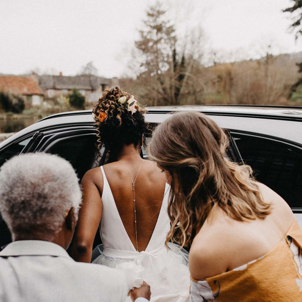 Bride in low back wedding dress with silver back chain wedding accessory getting into wedding car 