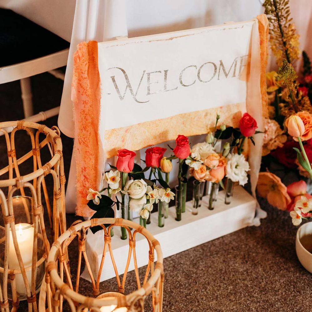 Wooden welcome wedding sign with orange frayed ribbon and test tube vase holders with garden roses and Iceland poppies 
