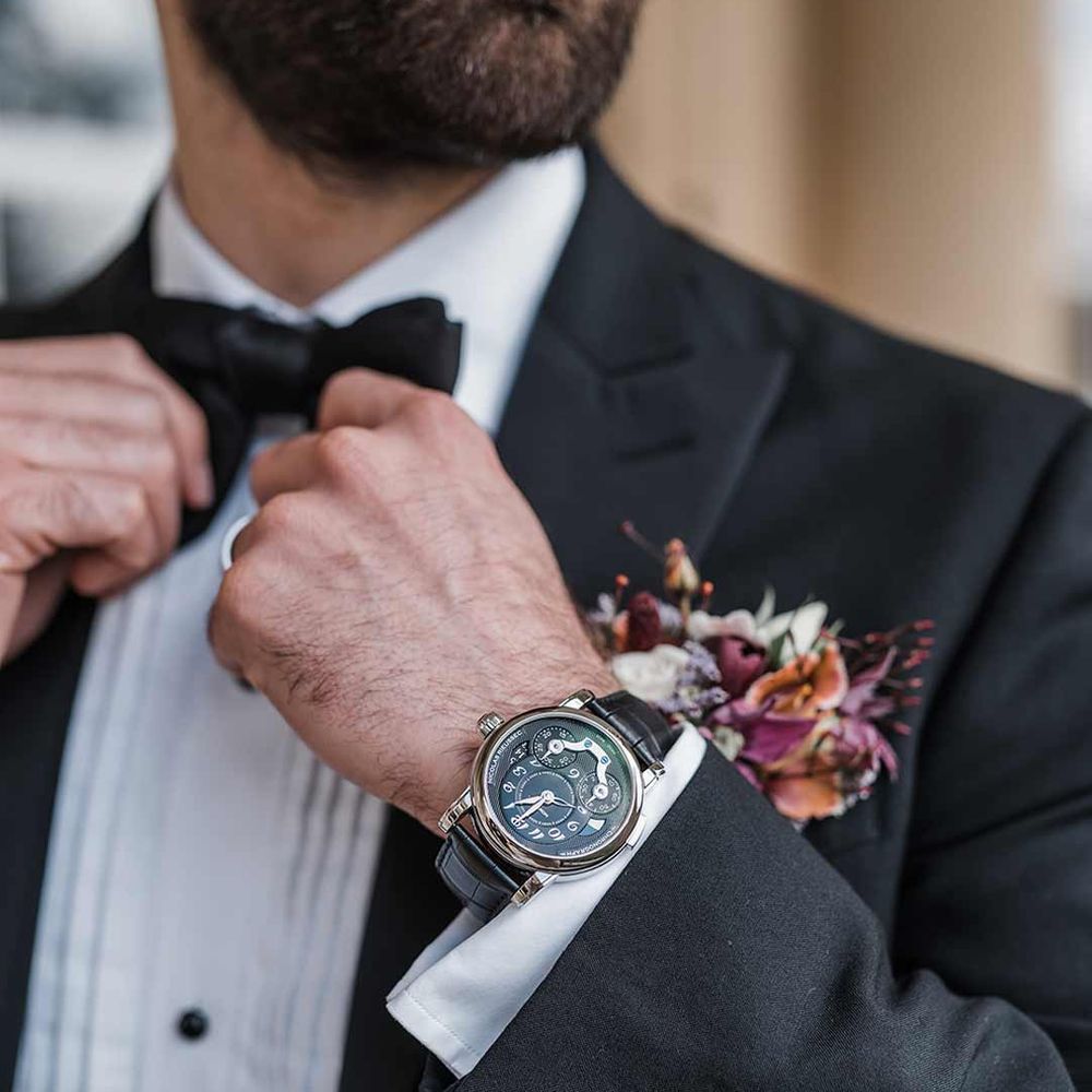 Stylish grooms accessories - Groom wearing gold and black watch, black bowtie, wildflower boutonniere and sleek classic black tuxedo