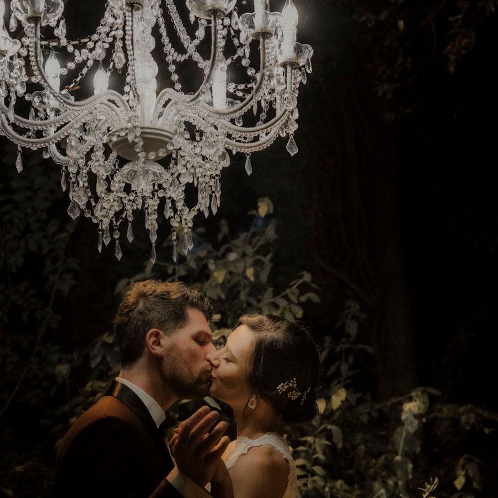 Bride and groom share a kiss under a stunning chandelier 