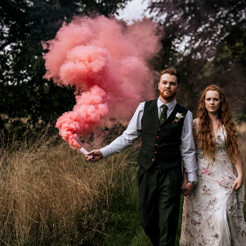 Bride & groom walk through the countryside with pink smoke bomb 