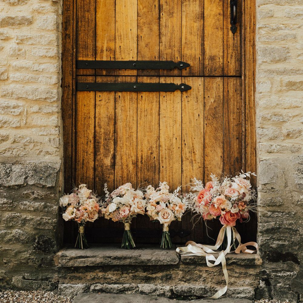 Pink and white rose wedding bouquets in front of rustic barn door at Tythe Barn Wedding