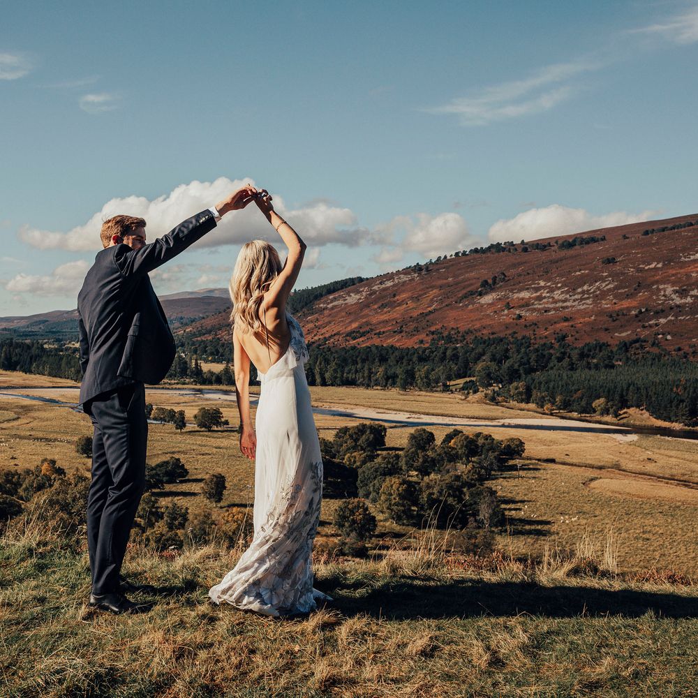Groom twirls bride in the Scottish countryside with hills in the background