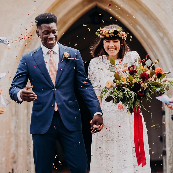Confetti moment with the bride in a Broderie Anglaise wedding dress and flower crown and groom in a navy suit 