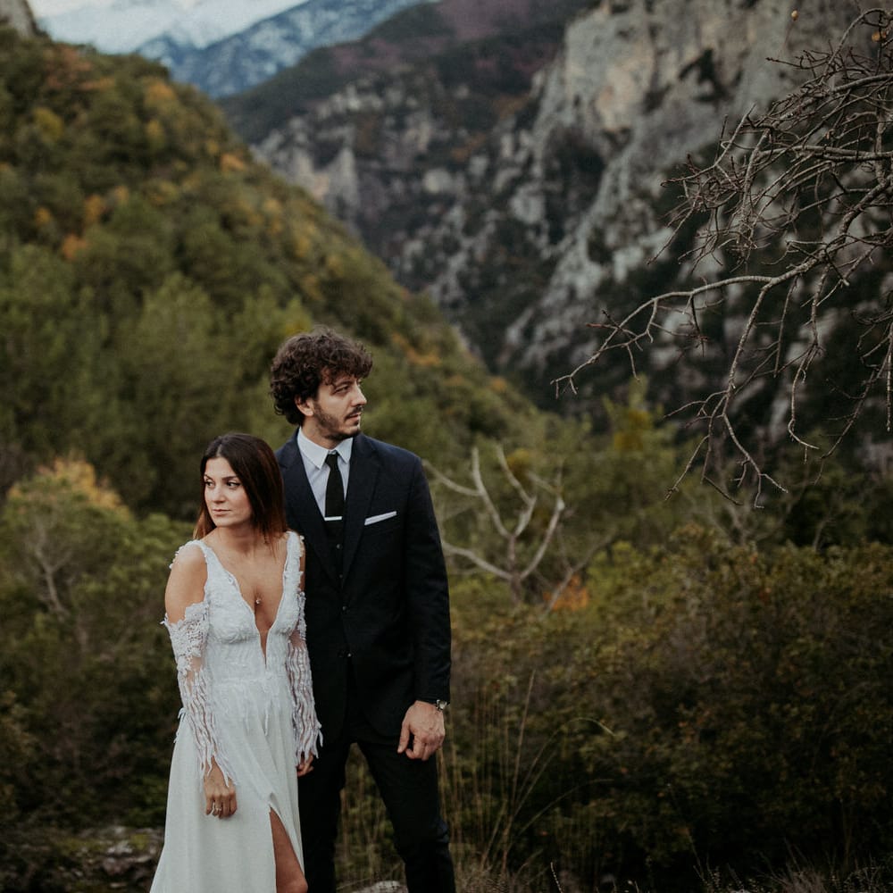The bride and groom pose next to each other in the green hills of Greece
