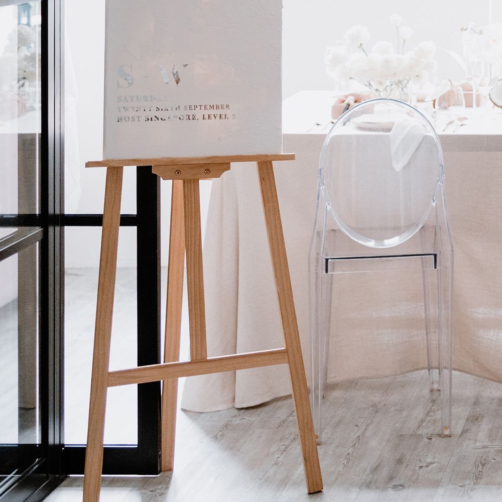 Minimalist wedding decor with white and silver foil welcome sign, ghost chairs and white flowers 