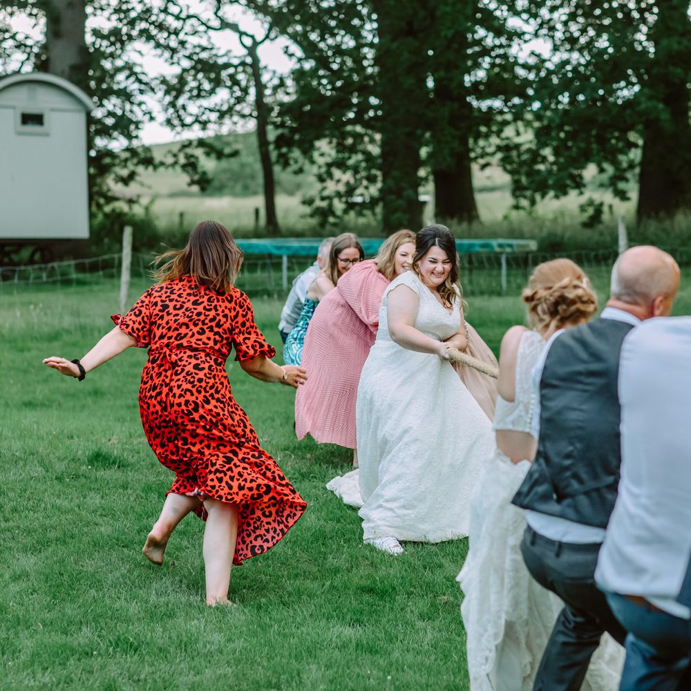 Brides play tug of war outdoors with wedding guests for garden games