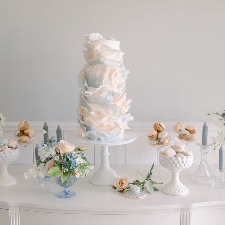 Dessert table with ombre pink and blue ruffle wedding cake, Choux buns and macaroons decorated with pastel flowers 