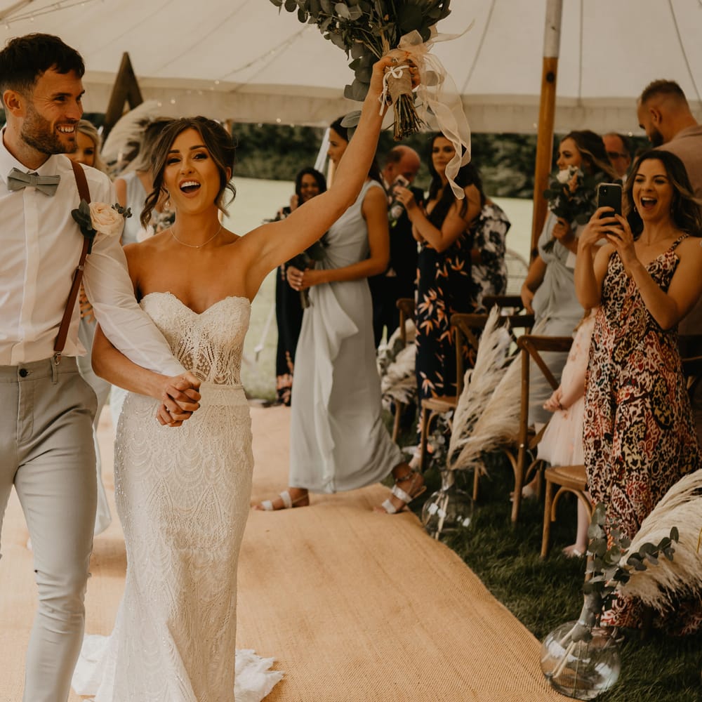 Bride & groom celebrate as they walk through marquee on their wedding day | Mark Bamforth Photography