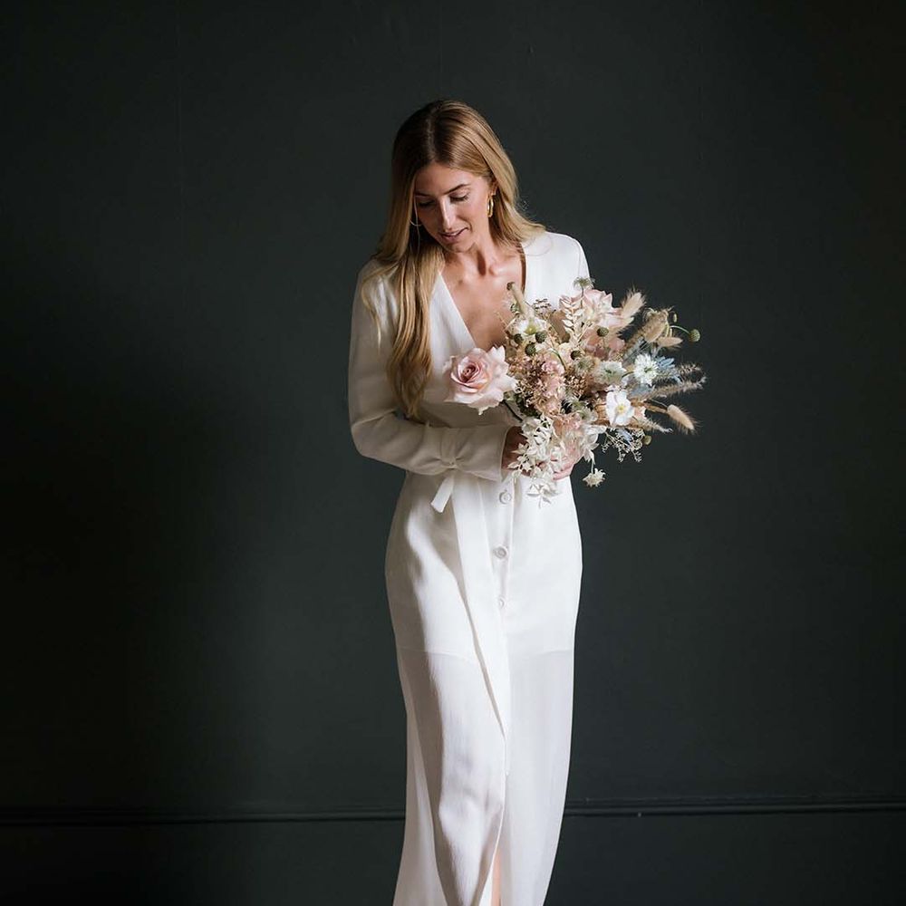 Bride in long sleeve buttoned white wedding dress with plunging neckline and gold mules